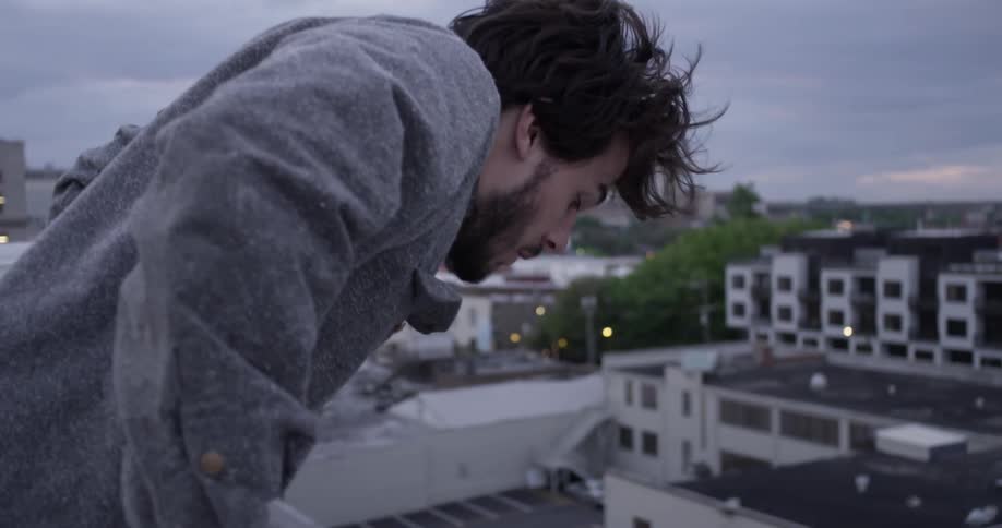A man leans over a rail on a rooftop