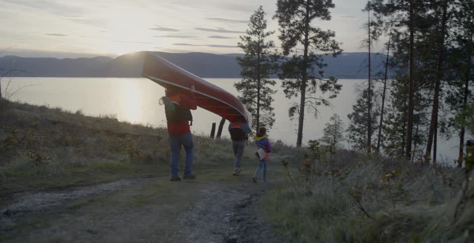 Two adults carry a canoe and a child walks by them towards the water