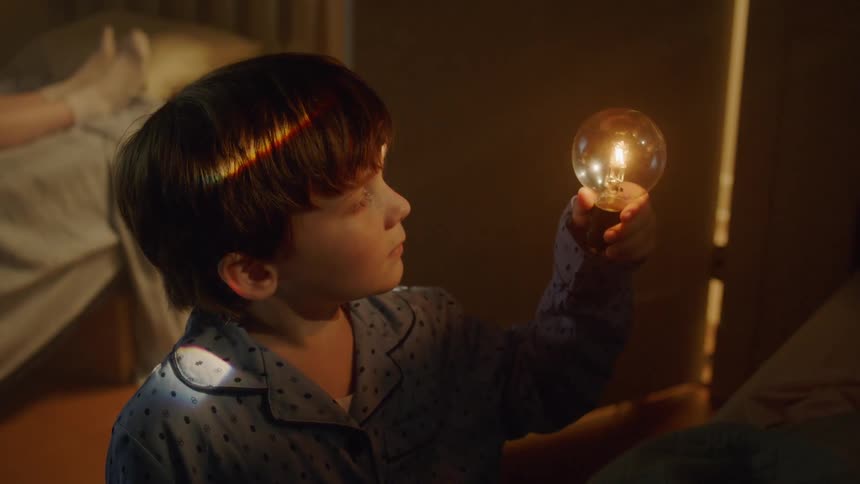 Boy looking at a lightbulb in a bedroom
