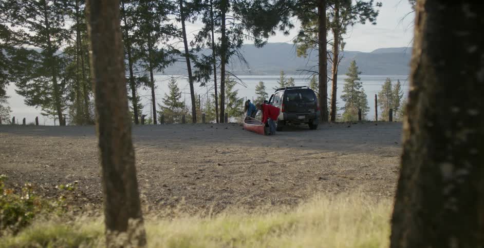 Family unloading a canoe off of a jeep near the water