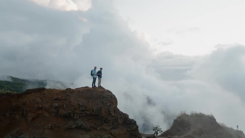 Two men are standing on mountain peak on cloudy day