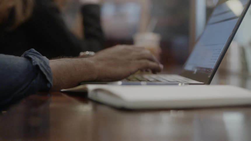 A man is working on a laptop inside a cafe