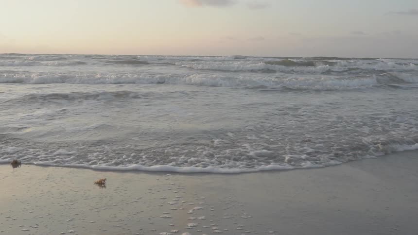 Waves are rolling onshore and receding from a beach at sunset