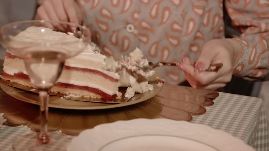 A woman uses a knife and fork to eat a large slice of cake