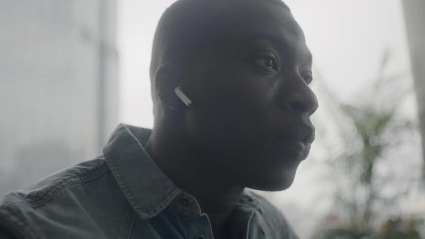 A man wearing wireless earbuds rubs his nose and talks