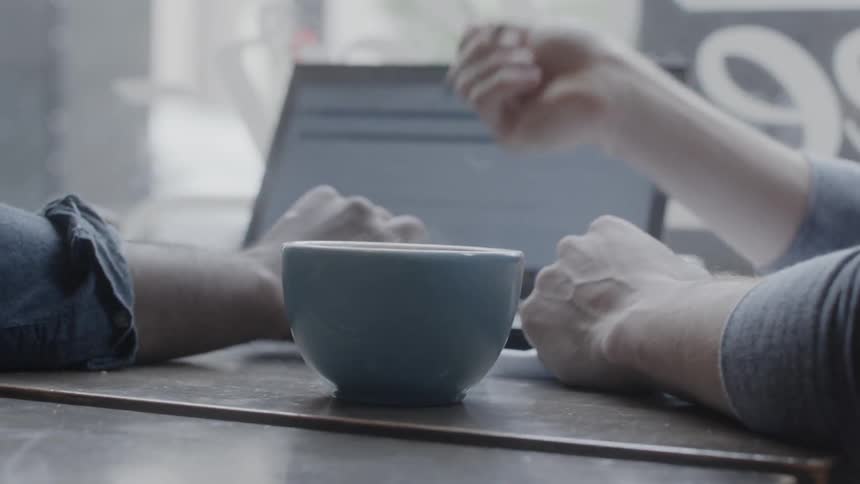 Two people sit in a coffee shop and work on a laptop