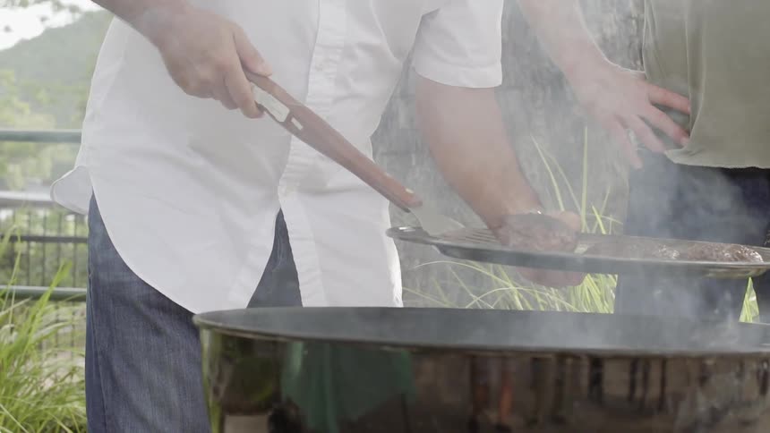 Men standing near a grill taking hamburgers off the grill