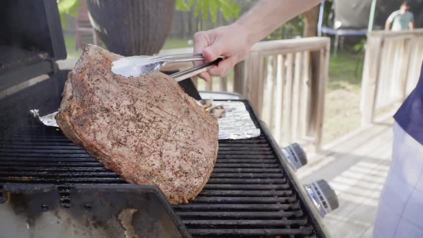 A man uses tongs to flip a steak on the grill