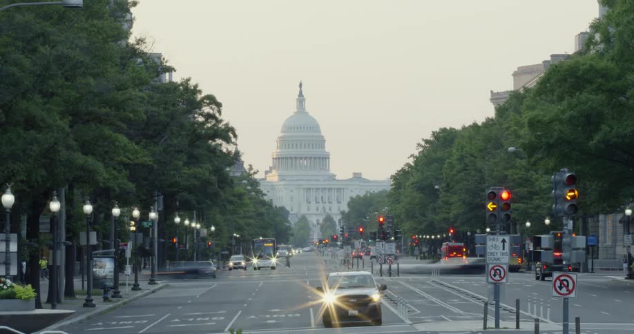 Cars drive on a street in front of a capitol building at sunrise
