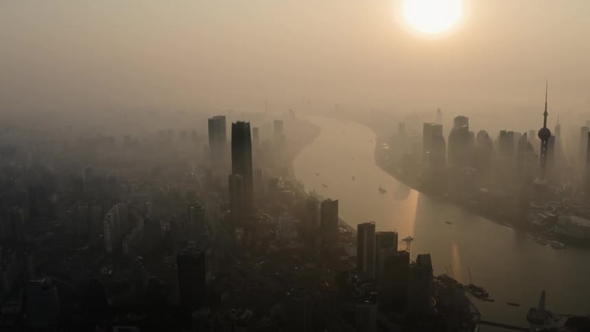 Haze is lingering in the air over a river wending through a city in daylight