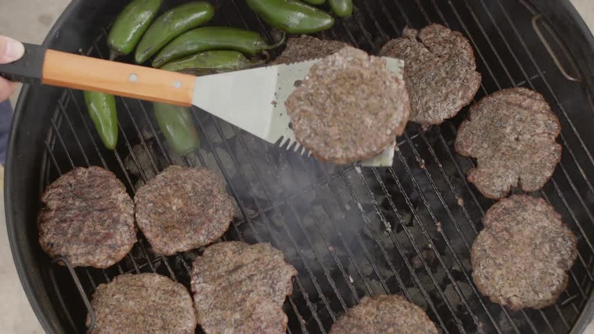 Hamburgers and peppers are cooked on a grill