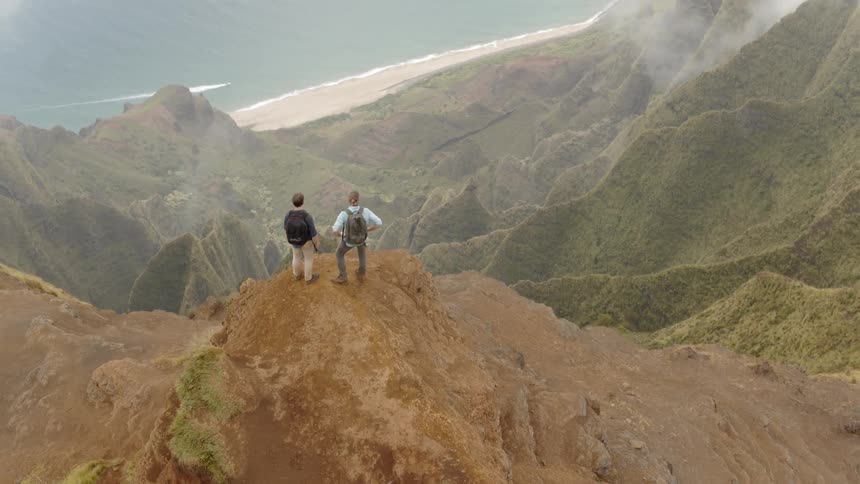 Hikers stand on a mountain peak overlooking a beach