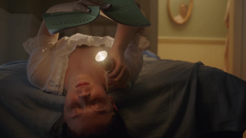 Young child lays on the bed as he shines a flashlight on a book