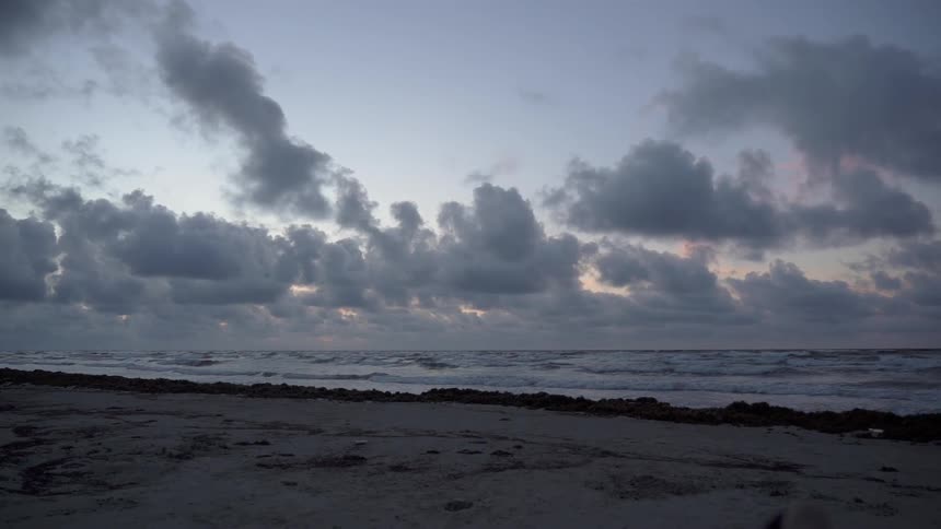 Waves coming ashore on a beach with a very cloudy sunset