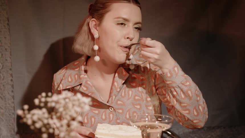 A woman is taking a bite of a slice of cake as she sits at a table