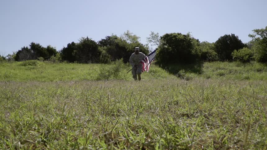 Army man is running with american flag in field on sunny day