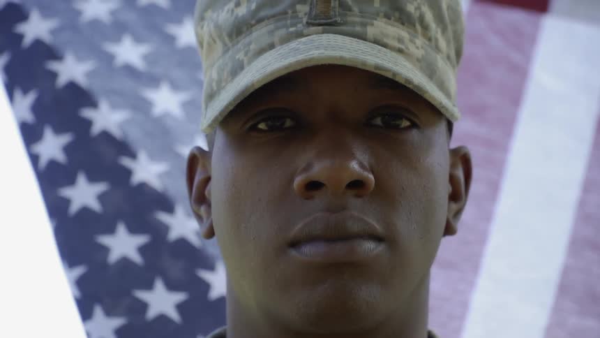 A soldier stands in front of a waving flag
