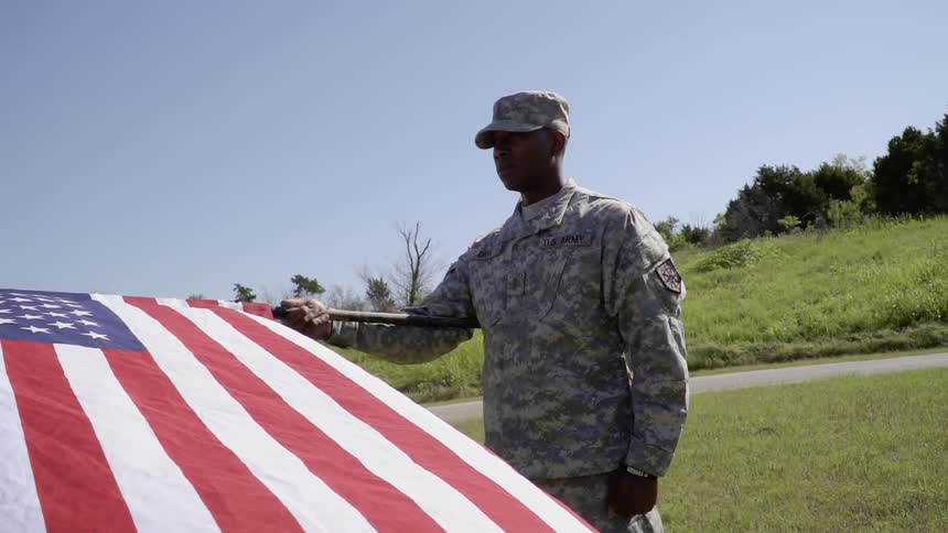 A soldier holds an american flag in a field
