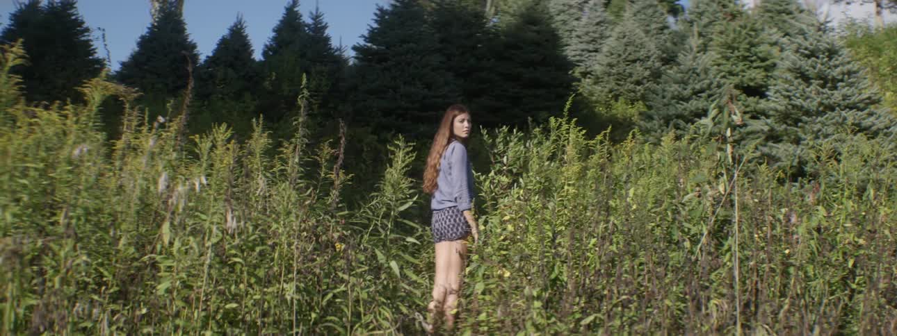 A woman walks through a forested area with tall weeds