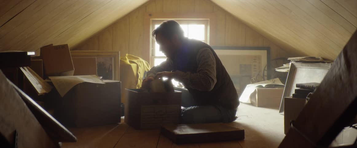 A man is going through a box in an attic in daylight