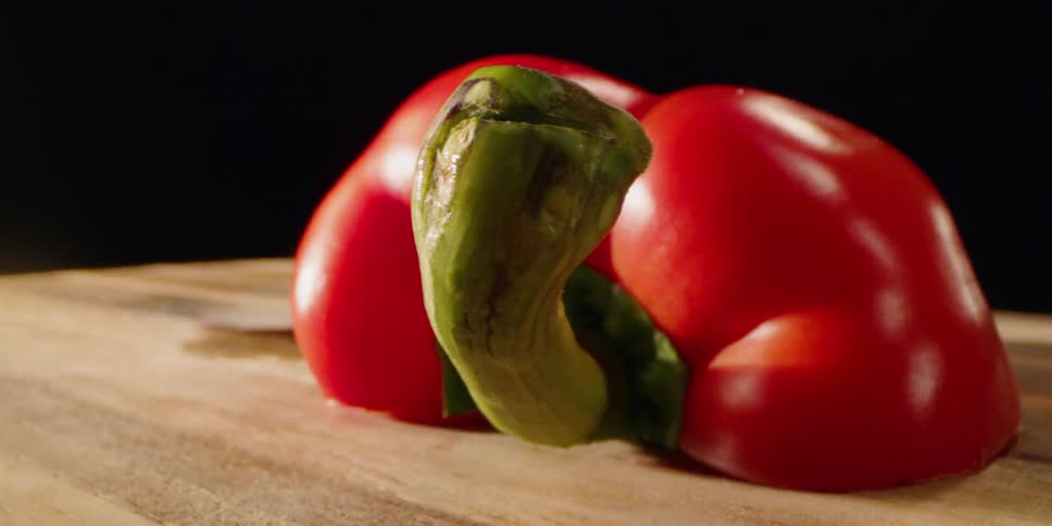 A pepper is sitting on a cutting board in daylight