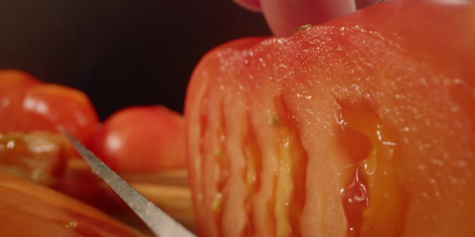 A knife is slicing through a tomato