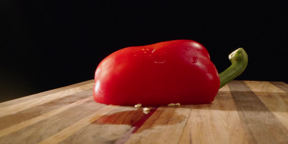 A halved red pepper sits on a wooden cutting board