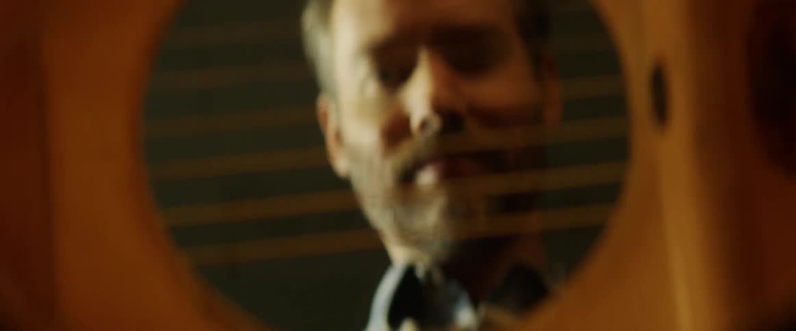 Man strums the strings of a guitar then nods his head and smiles