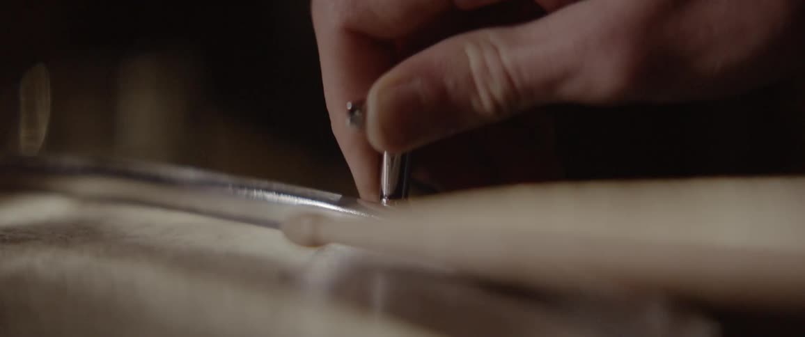 A drummer is tapping a drum as he sets it up inside in daylight