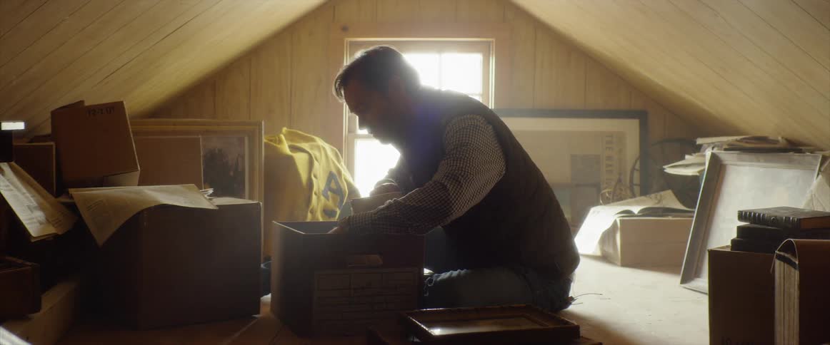 A man is digging through a box in the attic
