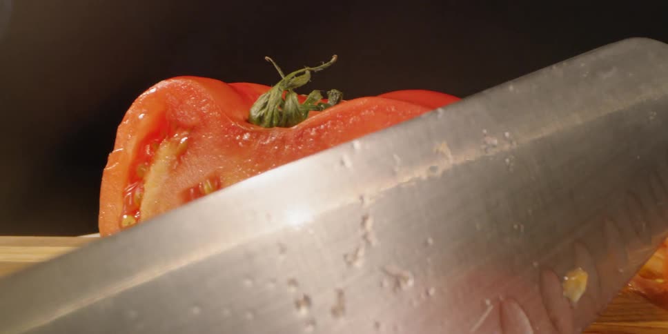 Knife leans against a sliced tomato on a cutting board