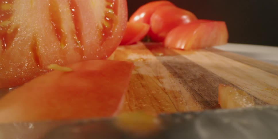 Half of tomato and slices on a wooden cutting board