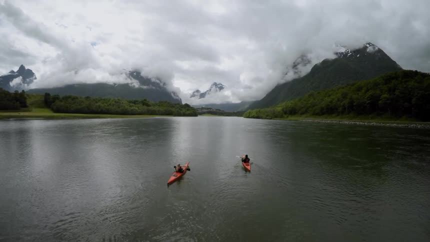 People kayaking on a body of water with cloud-covered, snow-capped mountains in the background