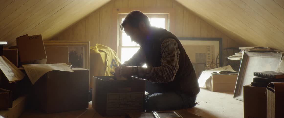 Man is sitting in attic and looking at keepsakes in box