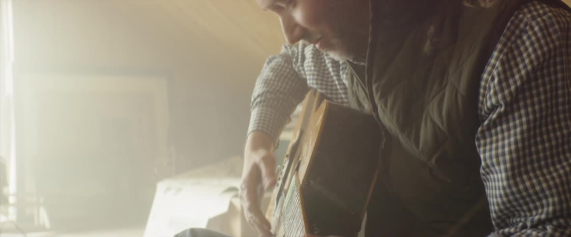 Man is sitting and playing guitar inside sunny room in house