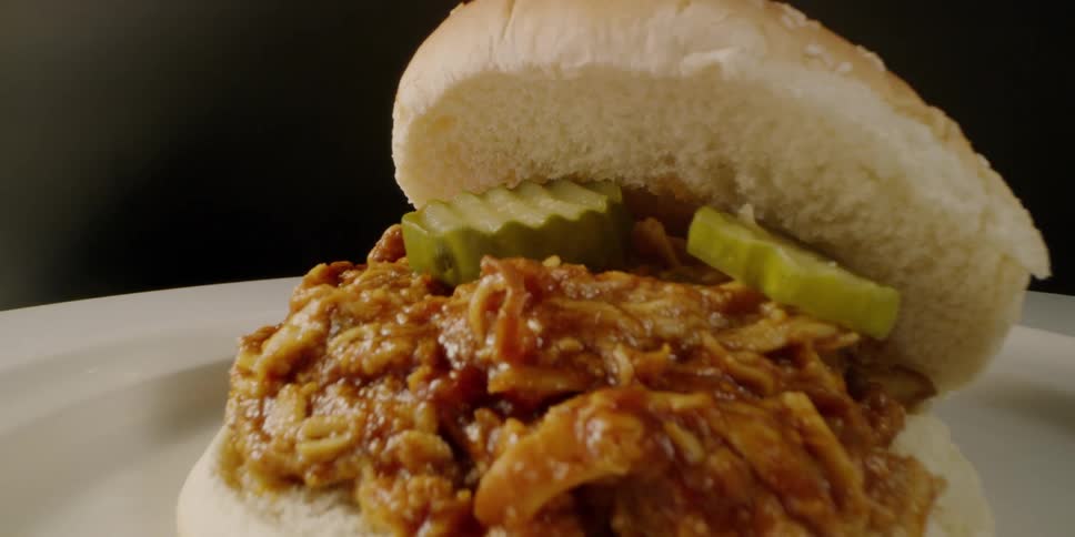 Pulled meat sandwich with pickles sits on a plate