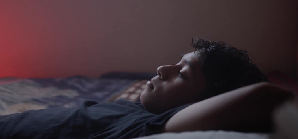 A boy lies on his bed with his hands beneath his head