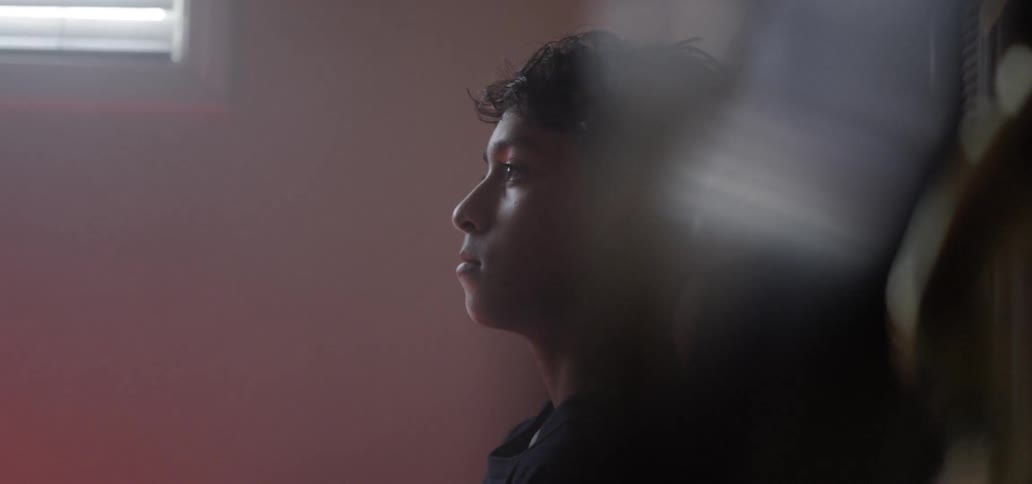 Teenager sits on a bed blank faced