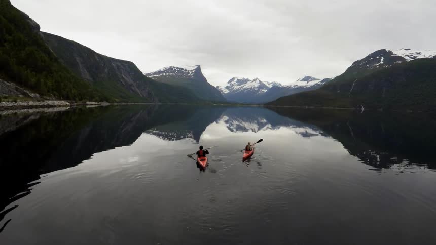 Kayakers paddle on a lake in front of the mountains