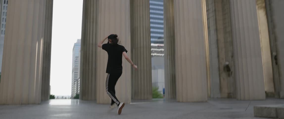 Woman does dance moves in front of a large building