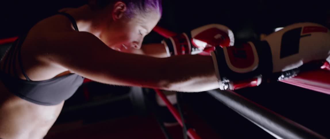 Woman leans against boxing ring ropes