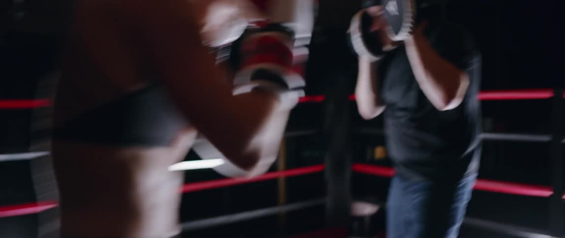 Woman practices punching a man's hands in a boxing ring