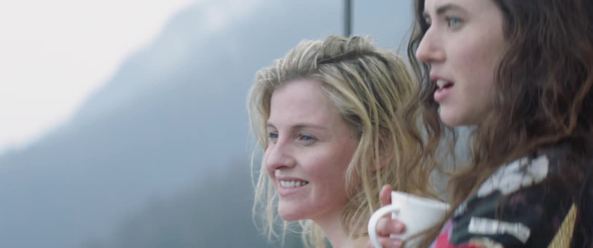 Women drink coffee on a balcony overlooking mountains