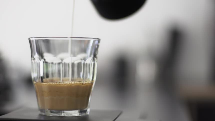 Someone pouring milk into a short coffee glass