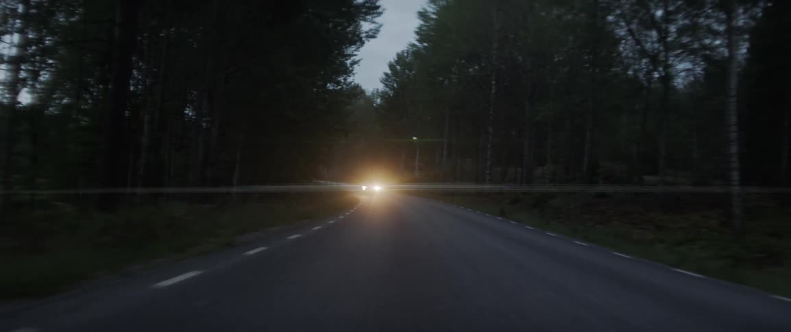 Headlights shine from a car driving down the road in the evening