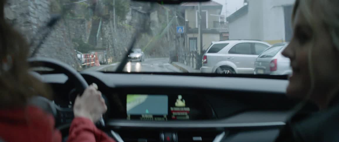 Two people ride in a car down a small road