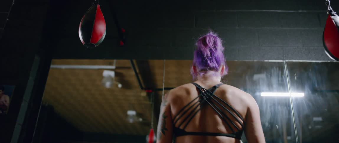 Woman with purple hair does stretches in a gym