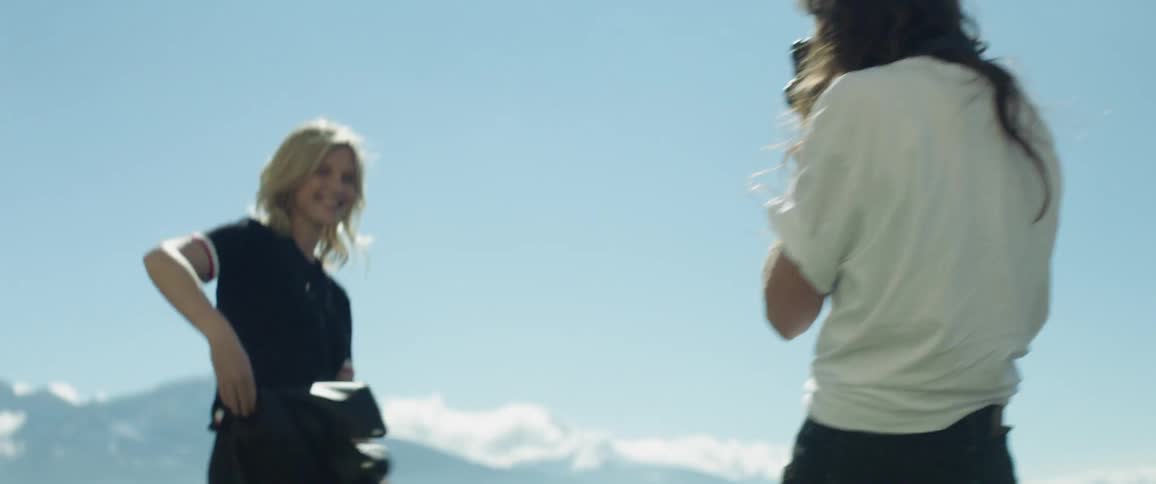 Woman smiles and takes her coat off while another takes a picture of her