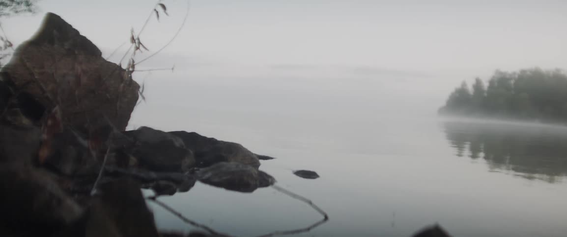 Rocks sit in the calm water under a cloudy sky