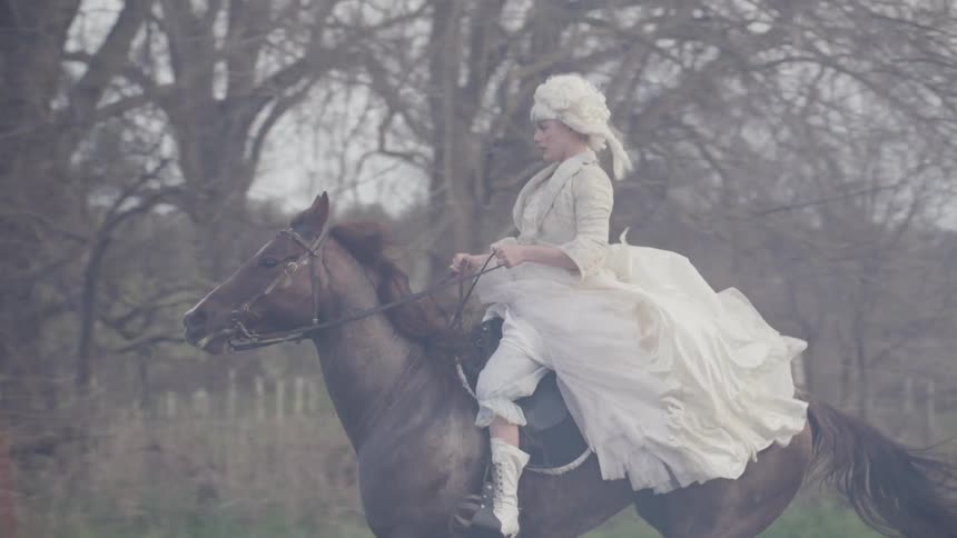 A woman rides a horse while wearing victorian era clothes